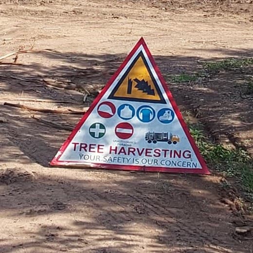 Triangular site sign reading Tree harvesting: your safety is our concern, with protective equipment symbols